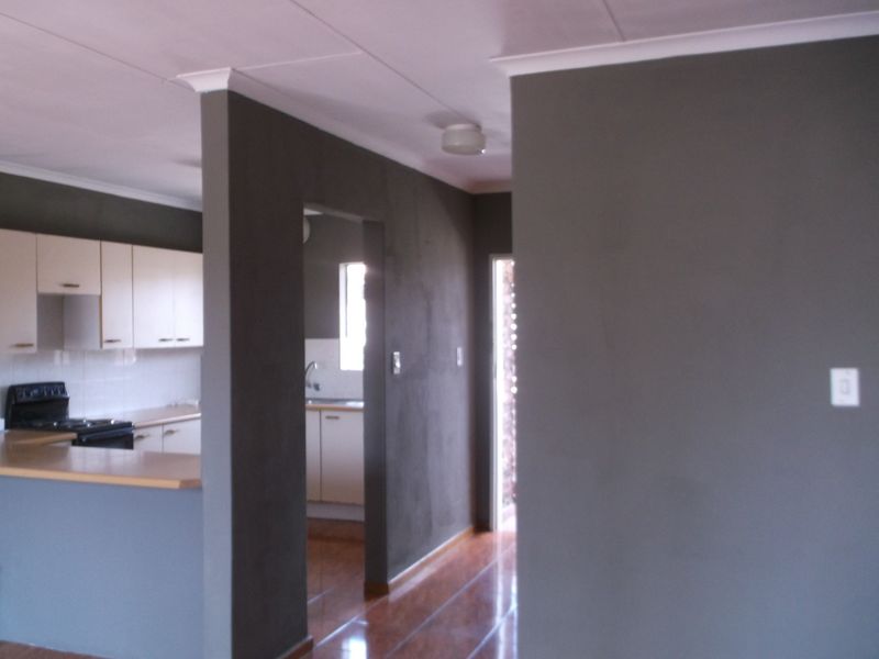 An open-plan living and kitchen area featuring laminate flooring, built-in cabinetry, and a neutral grey wall finish.