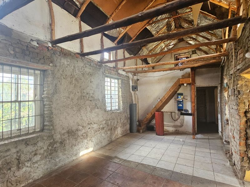 An interior view of a room in shell condition, featuring exposed timber roof beams, masonry walls, and tiled flooring, requiring significant renovation.