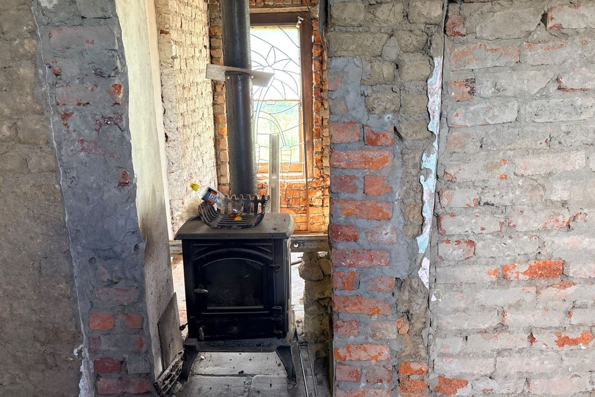 An interior space under renovation featuring exposed brick walls, a cast iron wood burning stove, and a decorative leaded glass window.