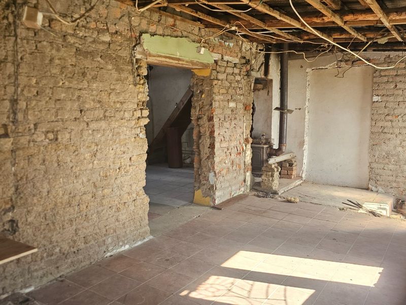A renovation-ready living space featuring exposed brick walls, tiled flooring, and exposed ceiling joists, offering a blank canvas for complete restoration.