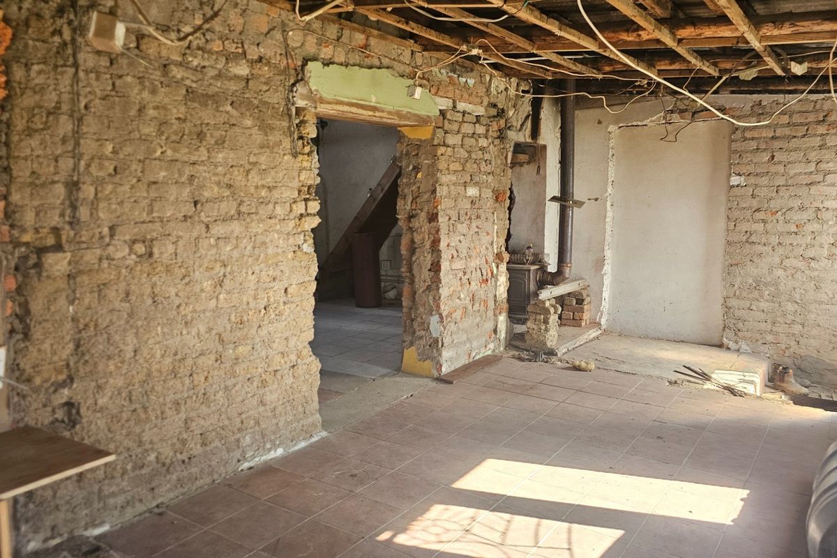 A renovation-ready living space featuring exposed brick walls, tiled flooring, and exposed ceiling joists, offering a blank canvas for complete restoration.