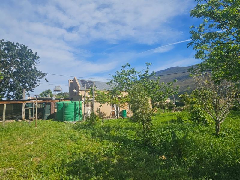 Rear view of the property featuring a garden, water storage tank, and solar water heating system set against a mountain backdrop.
