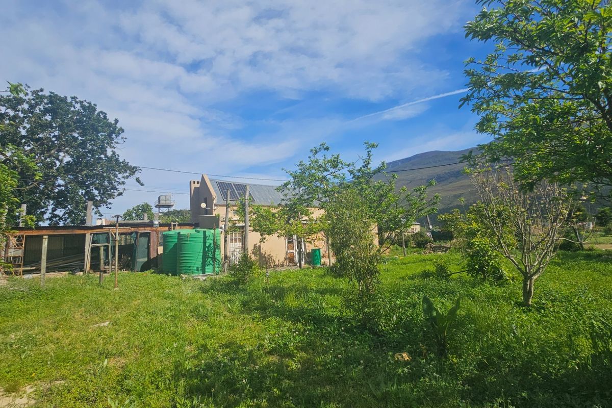 Rear view of the property featuring a garden, water storage tank, and solar water heating system set against a mountain backdrop.