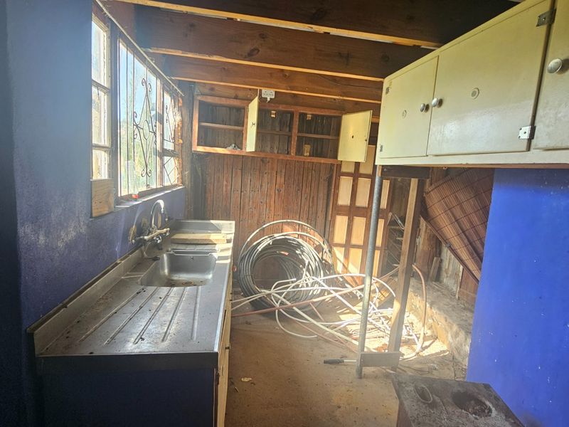 A utility or scullery area featuring a stainless steel sink, exposed timber beams, and built-in cabinetry, currently in need of significant renovation and repair.