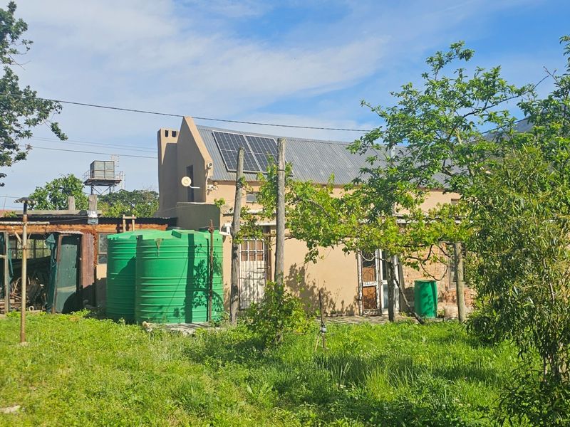Rear view of a rustic property featuring solar panels, water storage tanks, and a large garden area with mountain views.