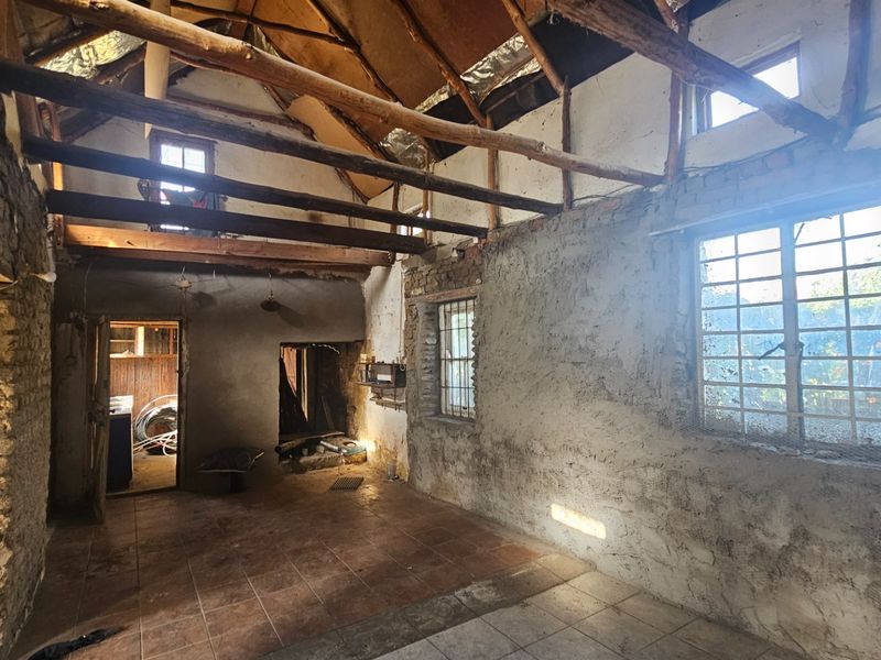 An unfinished interior space featuring exposed timber roof beams, tiled flooring, and raw brick and plaster walls, offering significant potential for renovation.