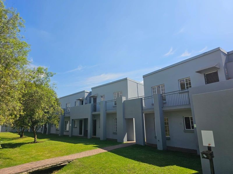 A view of the rear elevation of the townhouse complex, featuring grey painted facades, upper-level balconies with railings, and a well-maintained communal lawn.