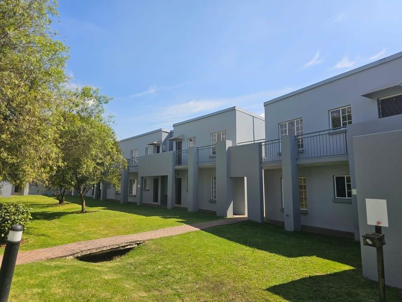 Exterior view of a multi-story townhouse complex featuring grey facades, upper-level balconies, and a well-maintained communal lawn with a paved pathway.