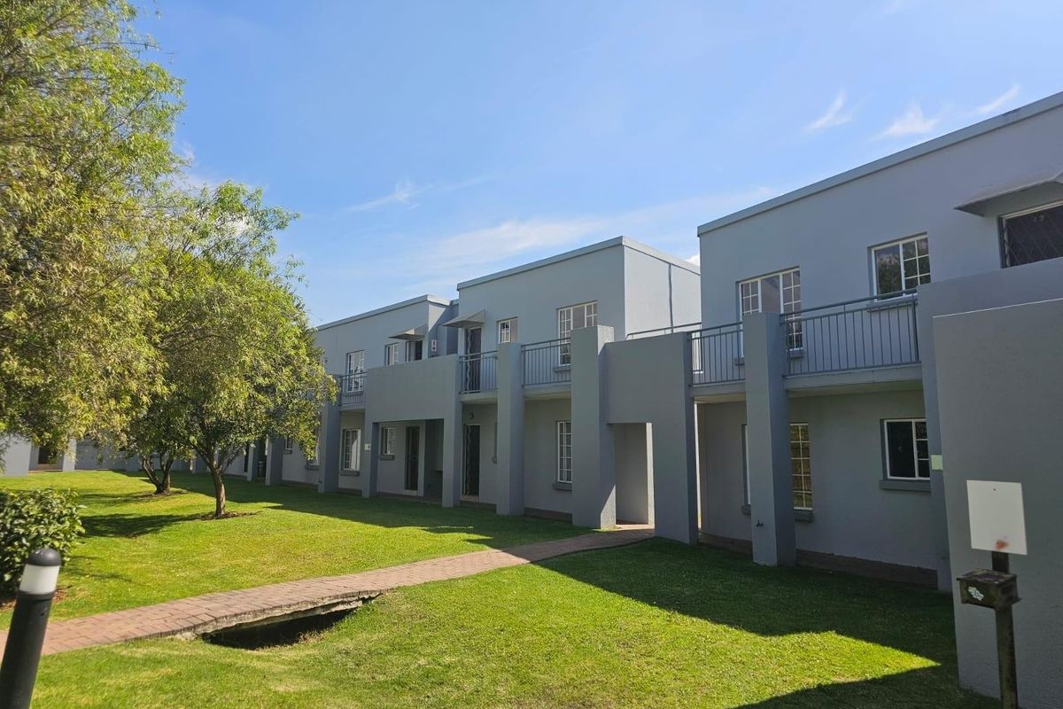Exterior view of a multi-story townhouse complex featuring grey facades, upper-level balconies, and a well-maintained communal lawn with a paved pathway.