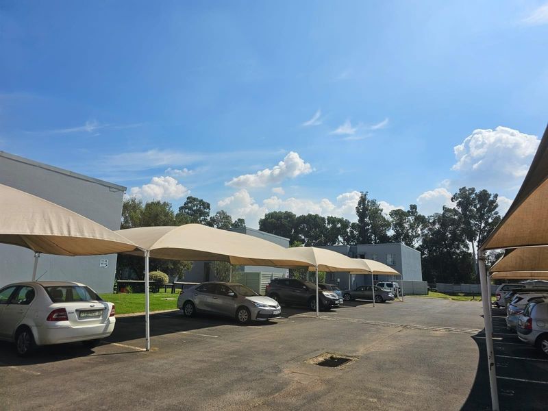 Exterior view of the townhouse complex parking area featuring multiple shade cloth carports and paved driveway.