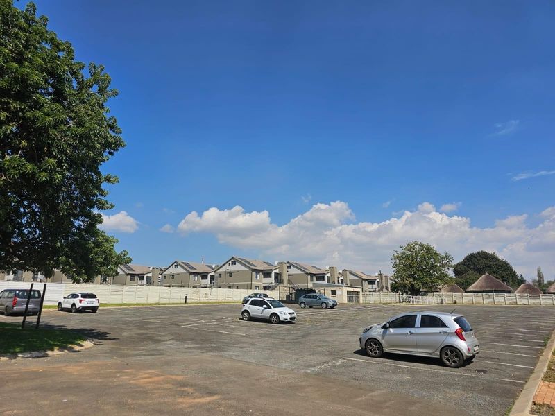 A wide-angle view of the townhouse complex parking area featuring paved surfaces and perimeter boundary fencing under a clear blue sky.