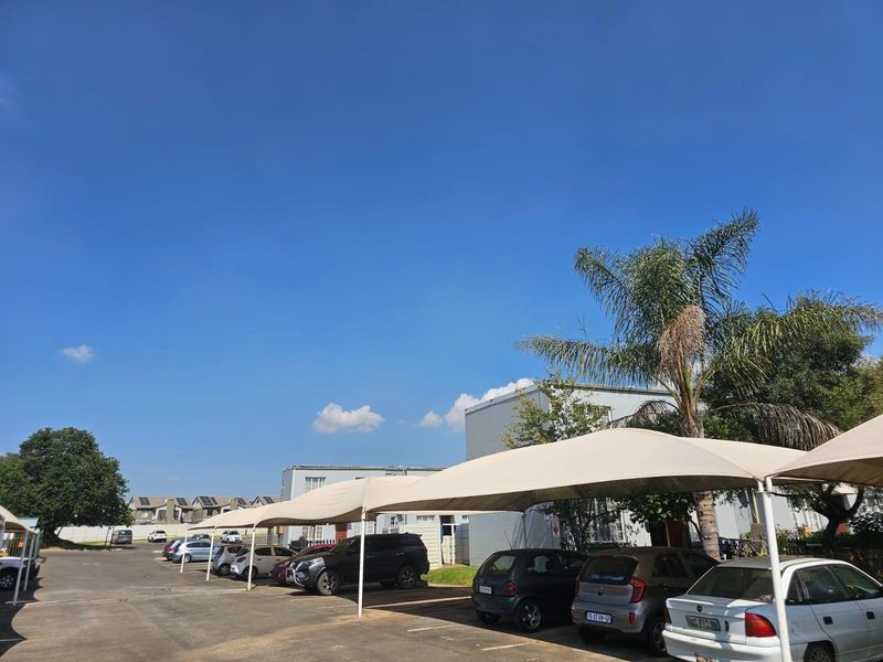 Exterior view of the townhouse complex featuring a paved parking area with multiple shade cloth carports for resident vehicle protection.