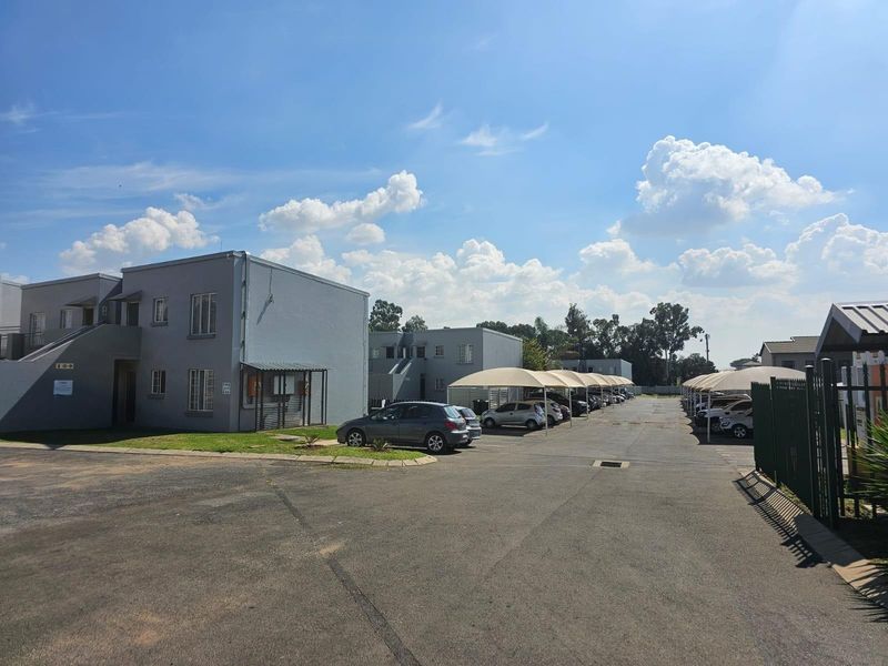 Exterior view of a townhouse complex featuring paved driveways, covered parking bays, and multi-story residential units.