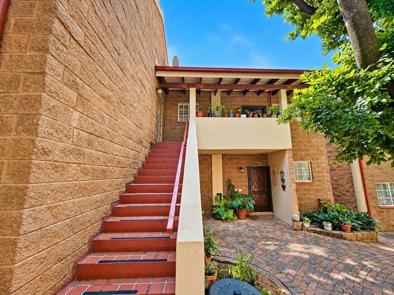 Exterior view of an apartment building featuring a brick facade, a tiled staircase leading to an upper balcony, and a paved ground-level courtyard.