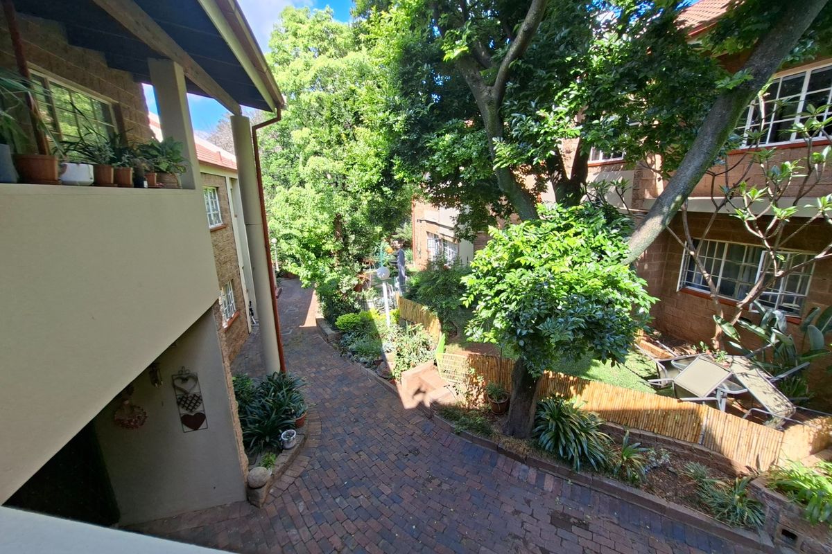 A view of the apartment complex rear exterior, featuring brick paved pathways, mature trees, and private balcony access.