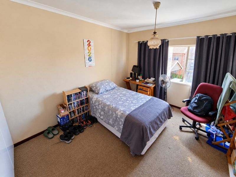 A functional bedroom featuring carpeted flooring, a central pendant light, and a window with curtain tracks.