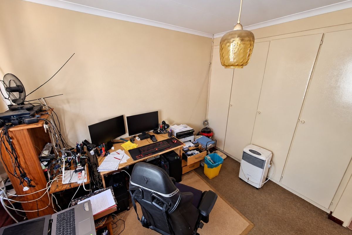 A bedroom featuring built-in cupboards, carpet flooring, and a pendant light fitting, currently utilized as a home office space.