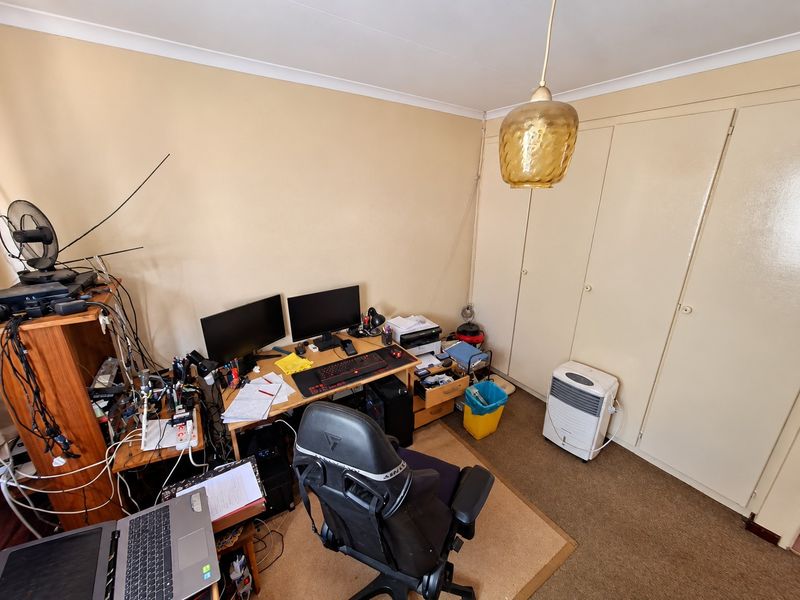 A bedroom featuring built-in cupboards, carpet flooring, and a pendant light fitting, currently utilized as a home office space.