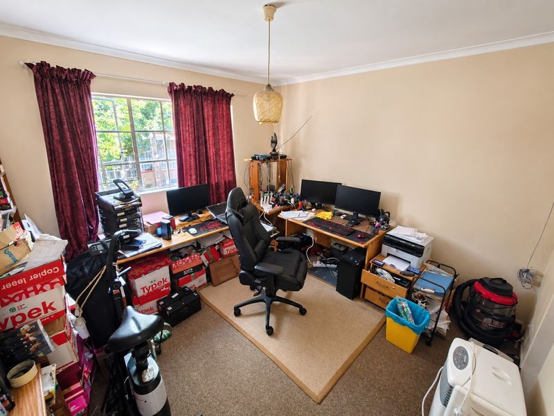 A functional home office space featuring carpeted flooring, a central pendant light, and a window with curtain tracks.