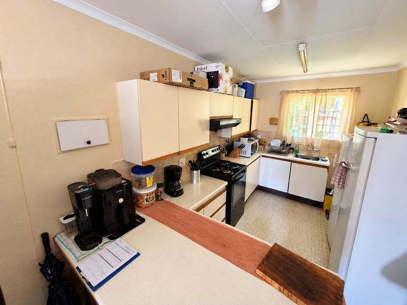 A functional kitchen featuring built-in cabinetry, a freestanding stove with extractor fan, and a stainless steel sink with tiled backsplash.