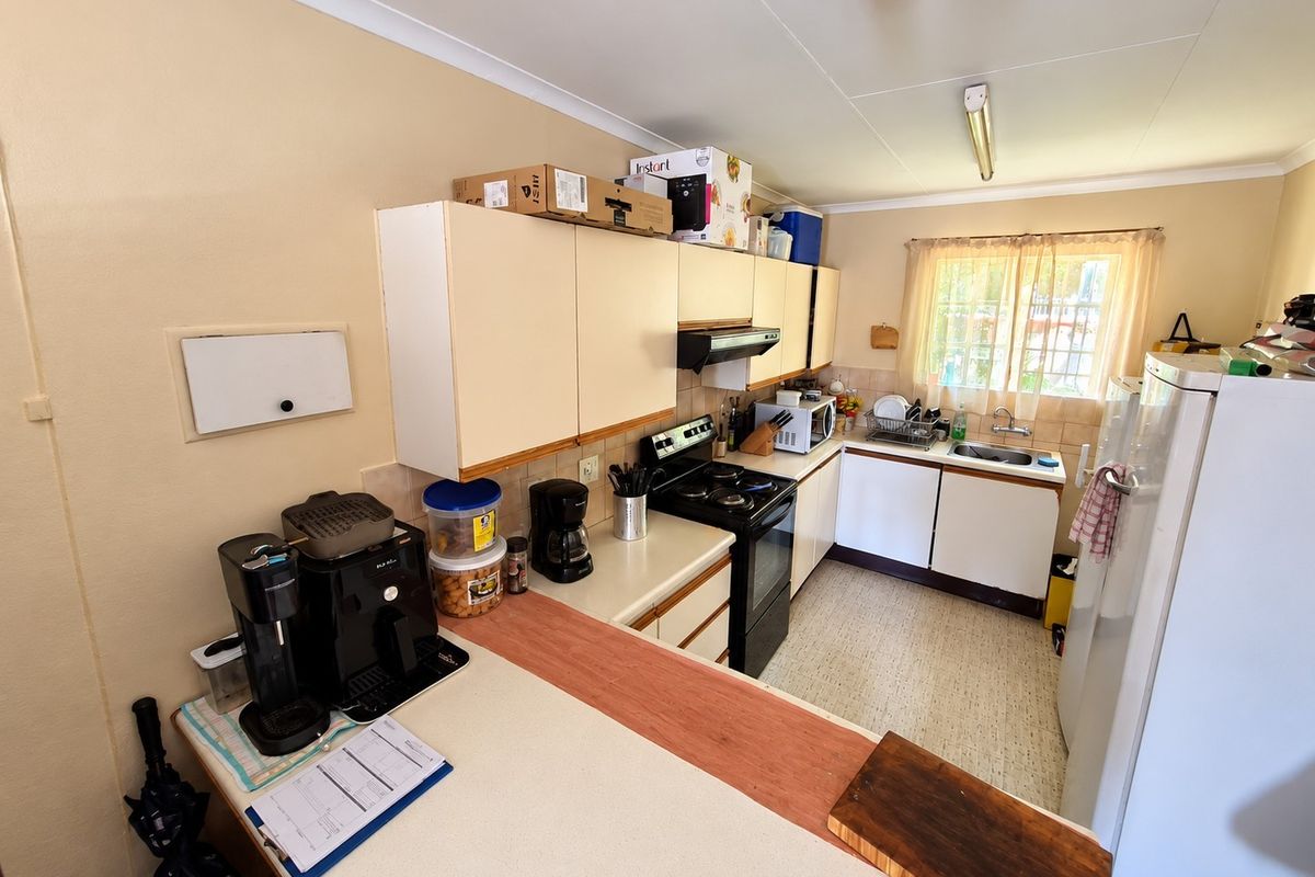 A functional kitchen featuring built-in cabinetry, a freestanding stove with extractor fan, and a stainless steel sink with tiled backsplash.