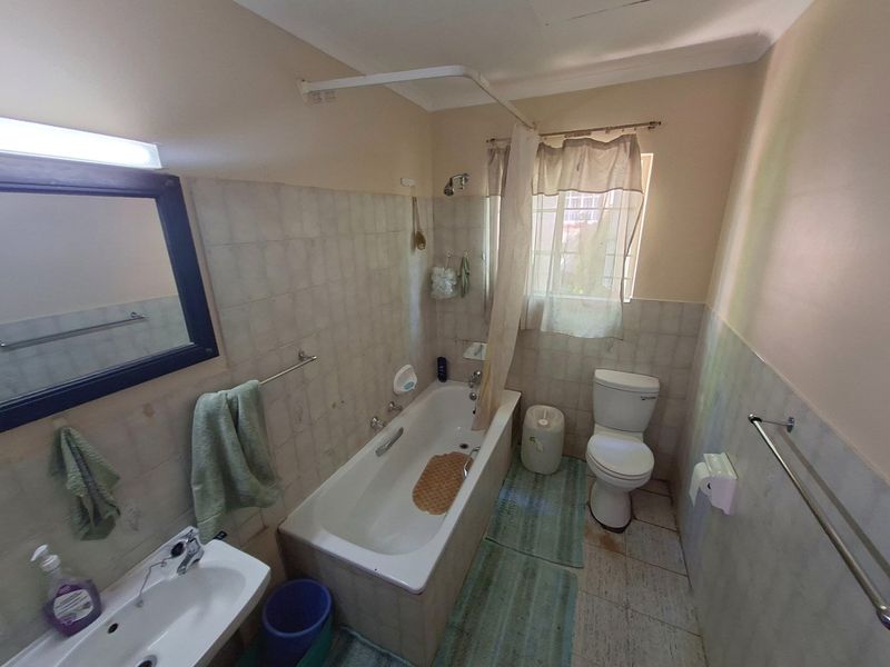 A functional bathroom featuring a bathtub with shower attachment, pedestal basin, and toilet, finished with neutral wall and floor tiling.