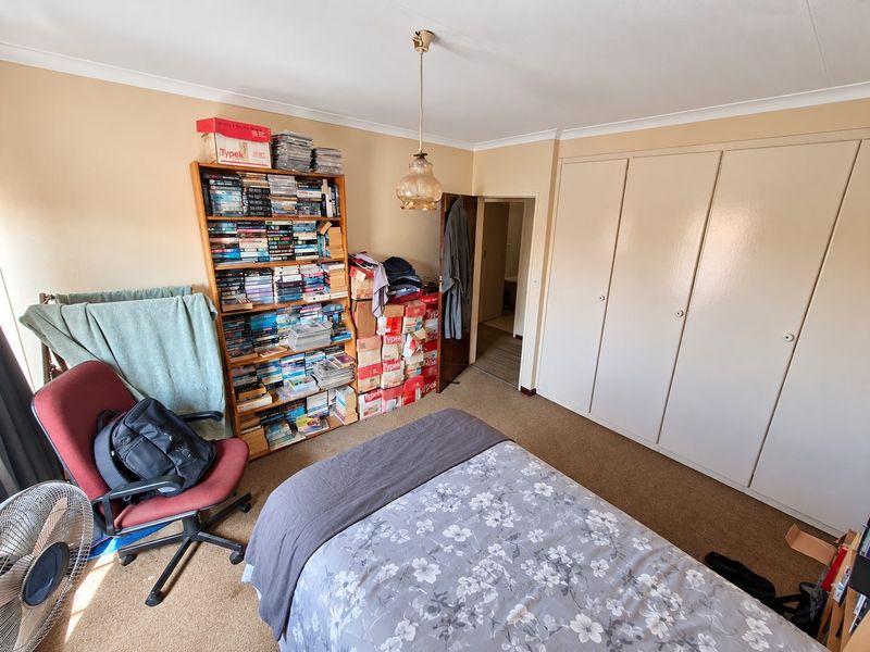 A bedroom featuring built-in cupboards, carpeted flooring, and a central pendant light fitting, offering a functional space with potential for modernization.