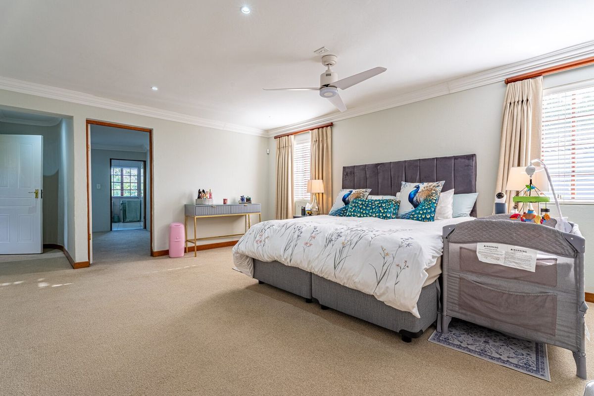 Spacious bedroom featuring neutral wall tones, crown molding, recessed lighting, a ceiling fan, and carpeted flooring with access to an adjoining room.