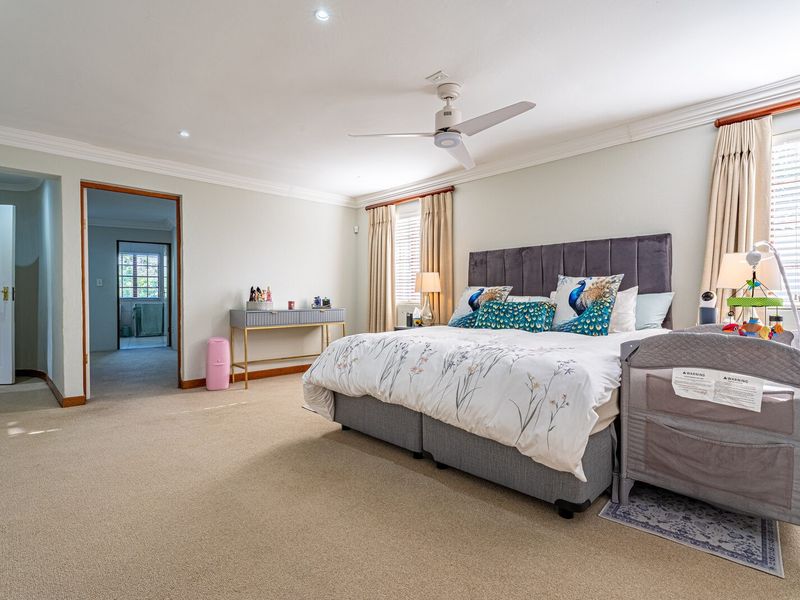 Spacious bedroom featuring neutral wall tones, crown molding, recessed lighting, a ceiling fan, and carpeted flooring with access to an adjoining room.