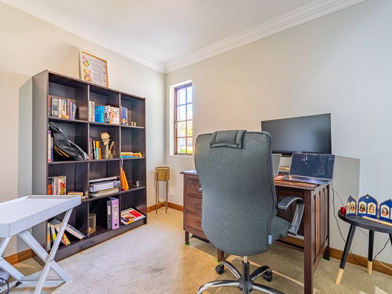 A functional home office featuring crown molding, neutral wall finishes, and a window providing natural light.