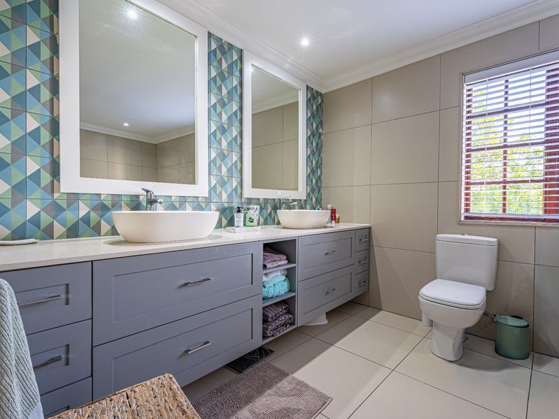 Modern bathroom featuring a double vanity with vessel sinks, patterned feature wall tiling, ample built-in cabinetry, and a private toilet area.
