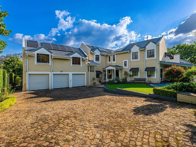 Spacious multi-level residence featuring a triple garage, solar panel installation, and a well-maintained cobblestone driveway set within a landscaped garden.
