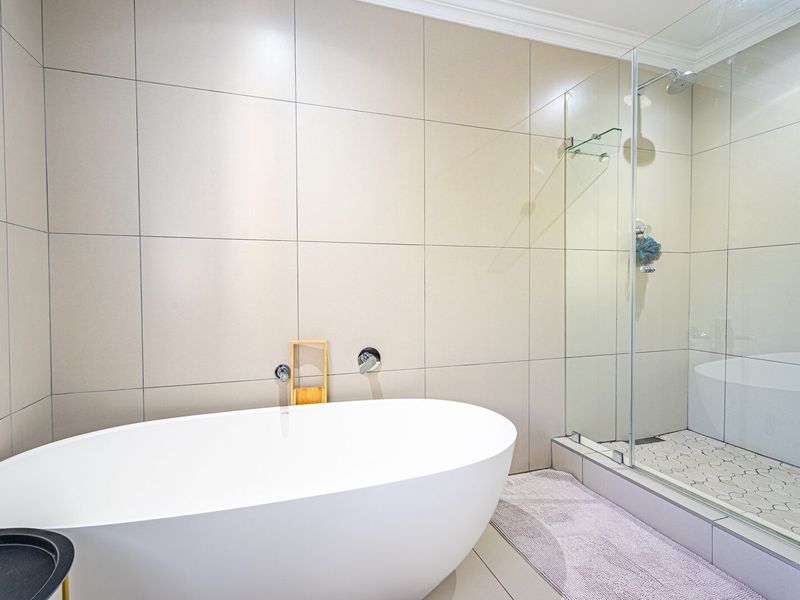 Modern bathroom featuring a sleek freestanding bathtub, a glass-enclosed shower with mosaic flooring, and neutral large-format wall tiles.