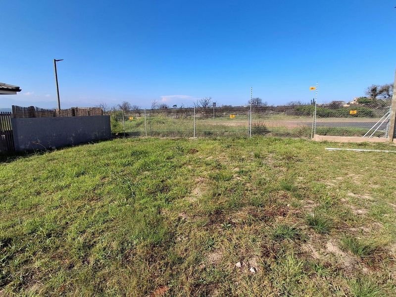A vacant residential plot featuring a grassed area, enclosed by a chain-link fence with electric security wiring and a concrete boundary wall.