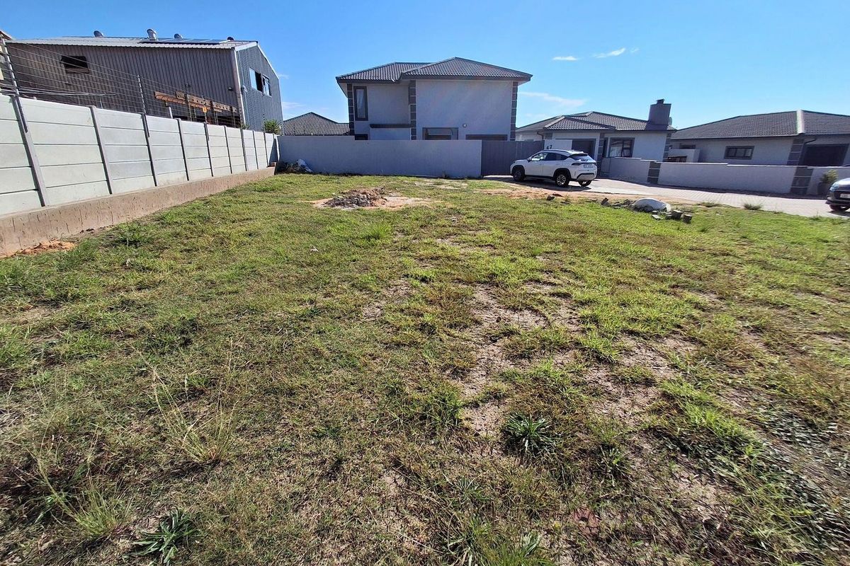 A vacant residential plot featuring a grassed area enclosed by precast concrete boundary walls in a developed suburban neighborhood.