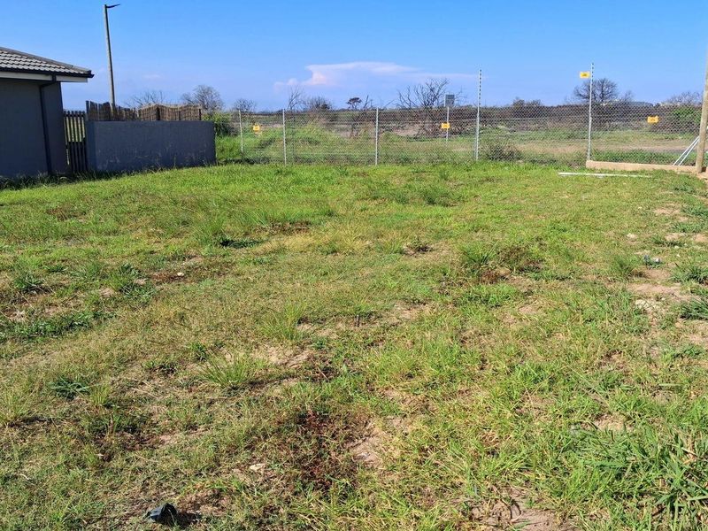A vacant residential plot featuring a grassed area enclosed by a chain-link fence and boundary wall with electric fencing.