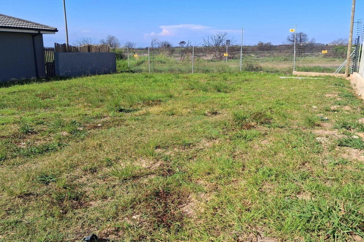A vacant residential plot featuring a grassed area enclosed by a chain-link fence and boundary wall with electric fencing.