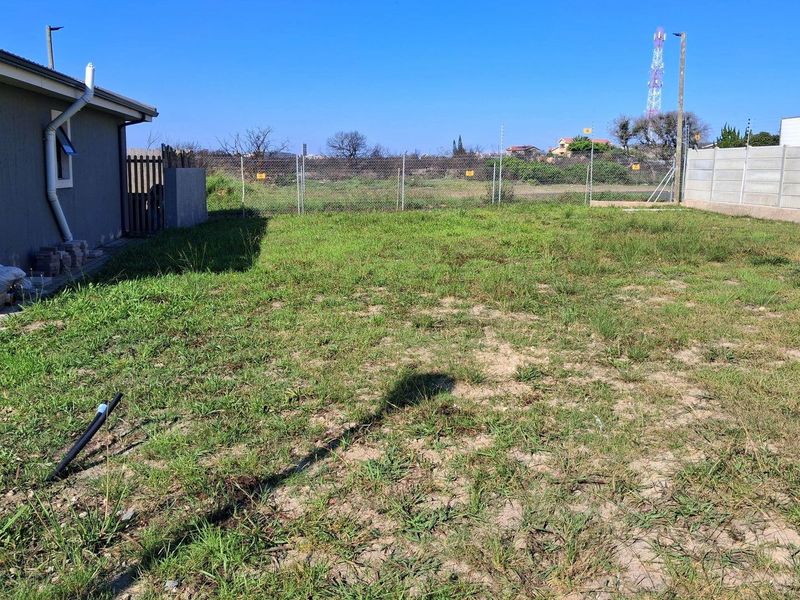 A view of the rear yard featuring a grass lawn, enclosed by a chain-link fence and a precast concrete boundary wall.