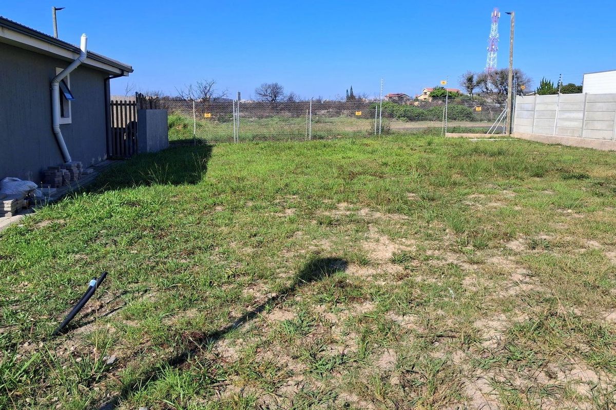 A view of the rear yard featuring a grass lawn, enclosed by a chain-link fence and a precast concrete boundary wall.