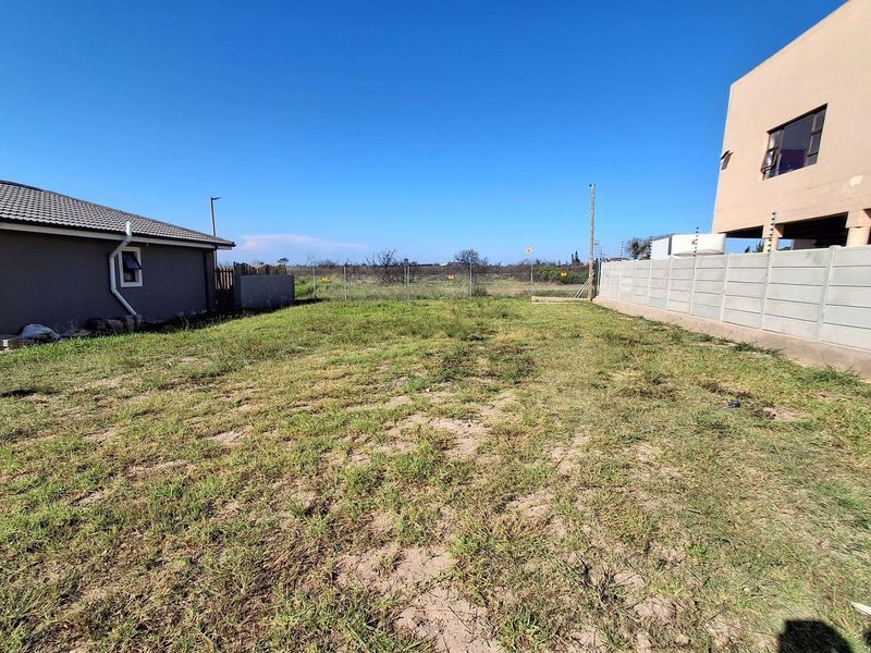 A view of the rear yard area featuring a grass lawn, enclosed by a precast concrete boundary wall and wire mesh fencing.