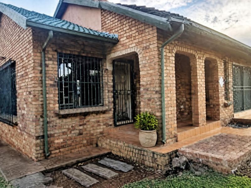 A single-story face brick house featuring a covered porch, security bars on windows, and a tiled roof, set on a paved and grassed plot.