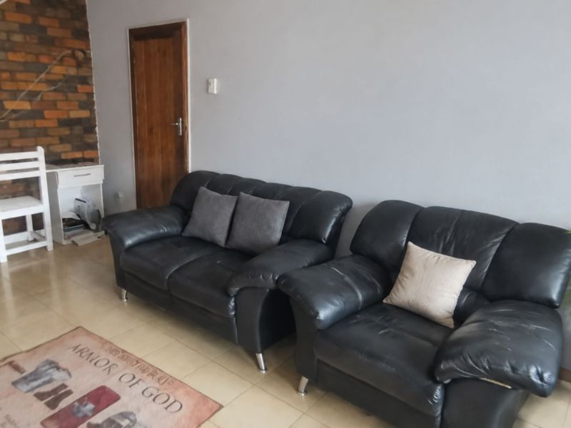 A living room featuring a rustic exposed brick accent wall, neutral tiled flooring, and a wooden door, offering a functional and comfortable living space.