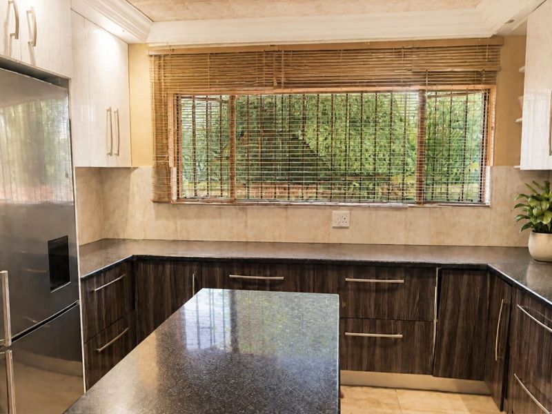 A well-maintained kitchen featuring dark wood cabinetry, granite countertops, a stainless steel refrigerator, and a window with security bars.