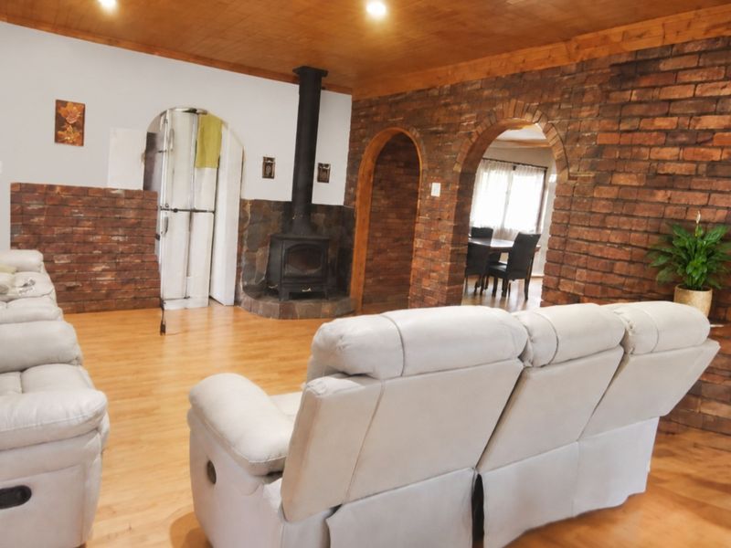 Spacious living room featuring exposed brick walls, a wood-burning fireplace, timber ceiling, and arched architectural details leading to adjacent living spaces.