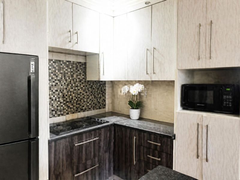 Compact kitchen featuring two-tone cabinetry, mosaic tile backsplash, dark laminate countertops, and integrated microwave and hob.