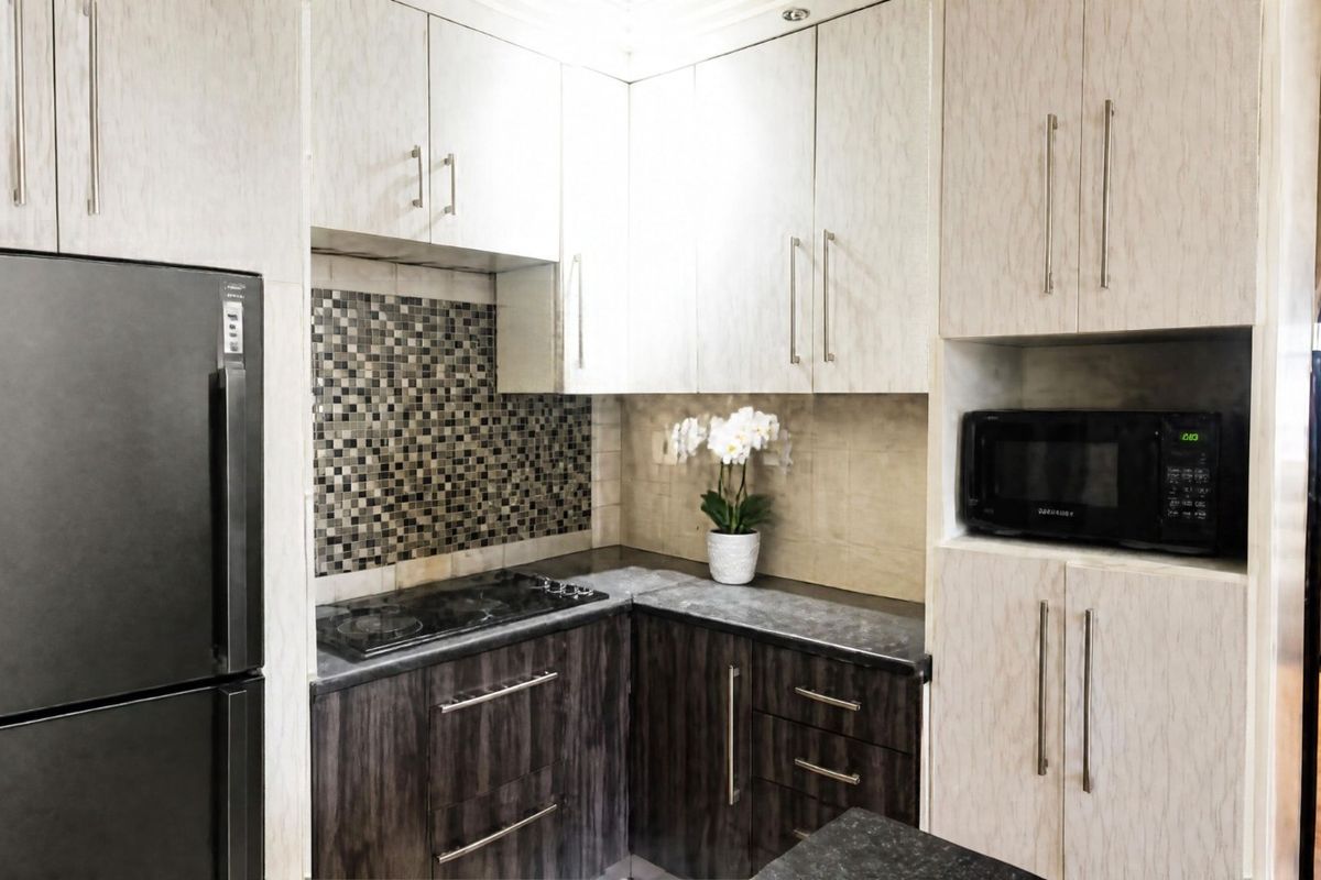 Compact kitchen featuring two-tone cabinetry, mosaic tile backsplash, dark laminate countertops, and integrated microwave and hob.