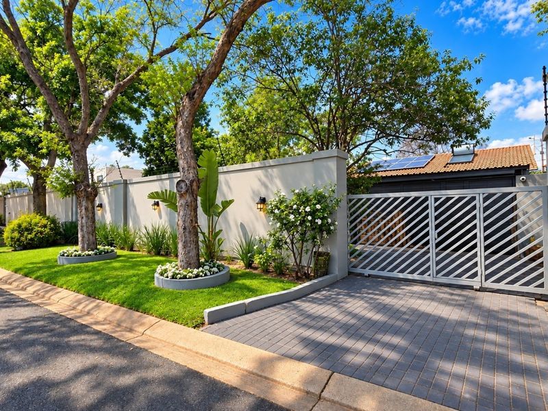 Well-maintained front exterior featuring a paved driveway, secure metal gate, perimeter wall with electric fencing, and established garden landscaping.