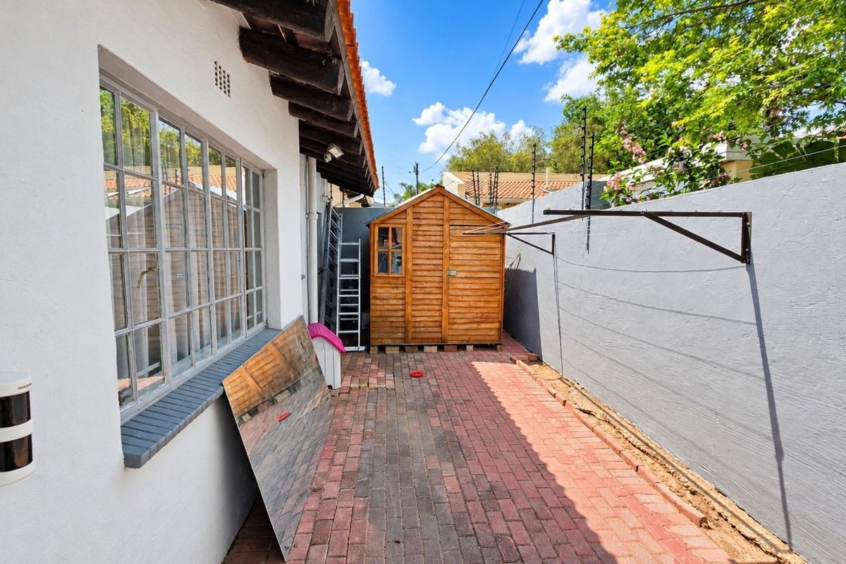 A paved rear exterior area featuring a timber garden shed, boundary wall, and wall-mounted clothesline, providing functional outdoor utility space.