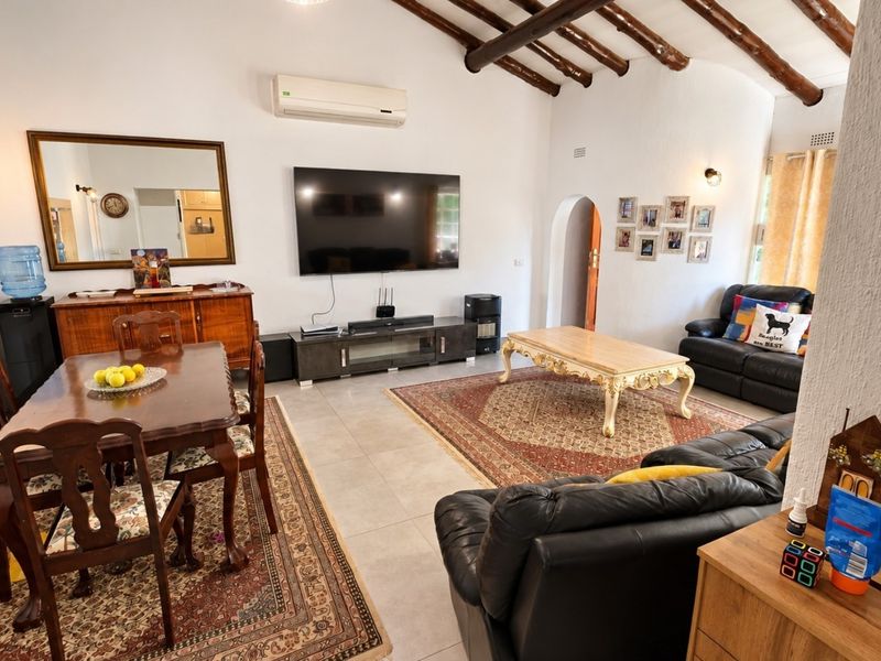 Spacious open-plan living and dining area featuring exposed timber ceiling beams, tiled flooring, and an arched doorway leading to other parts of the home.