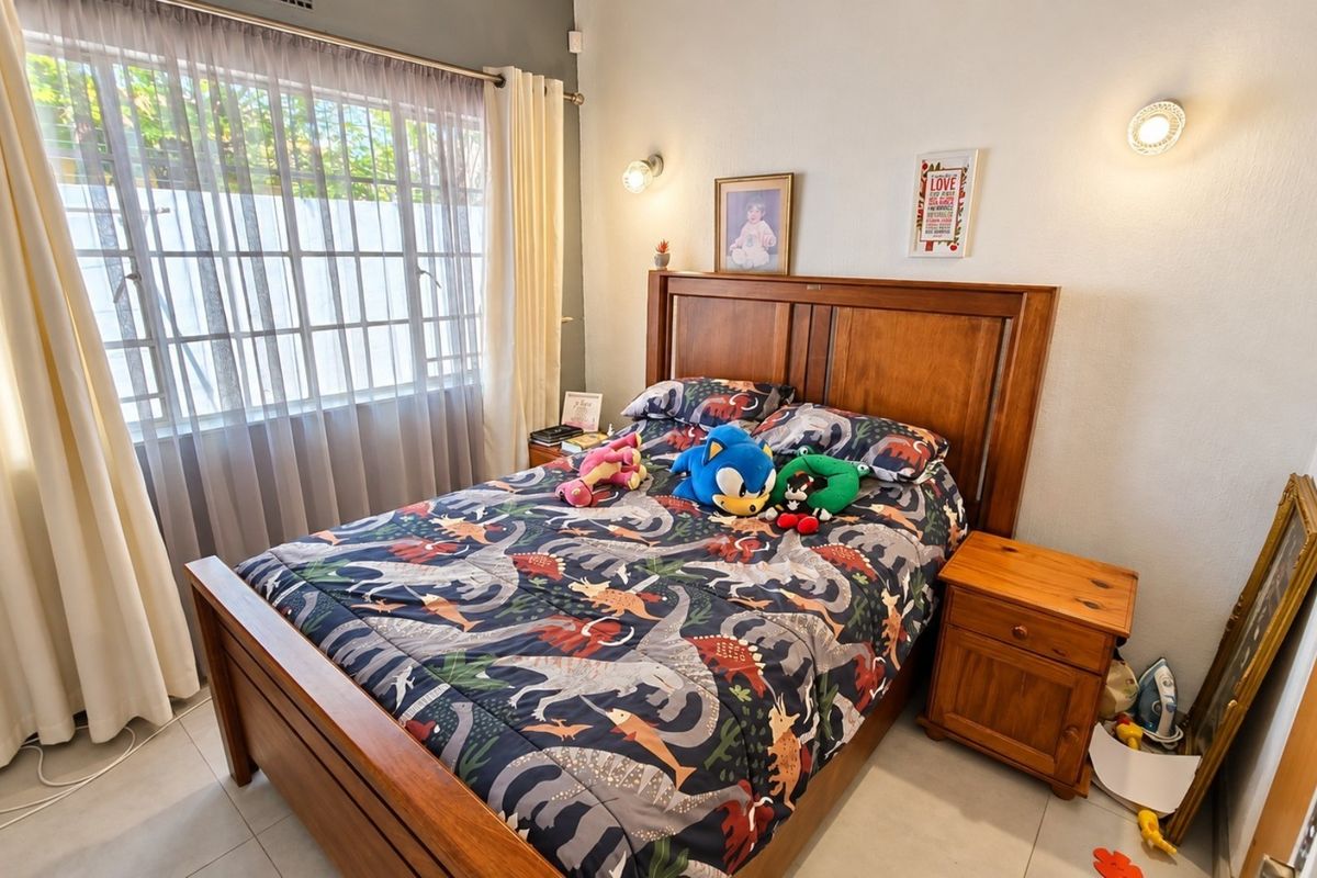 A well-maintained bedroom featuring tiled flooring, wall-mounted lighting, and a window with security bars, providing a functional and comfortable living space.